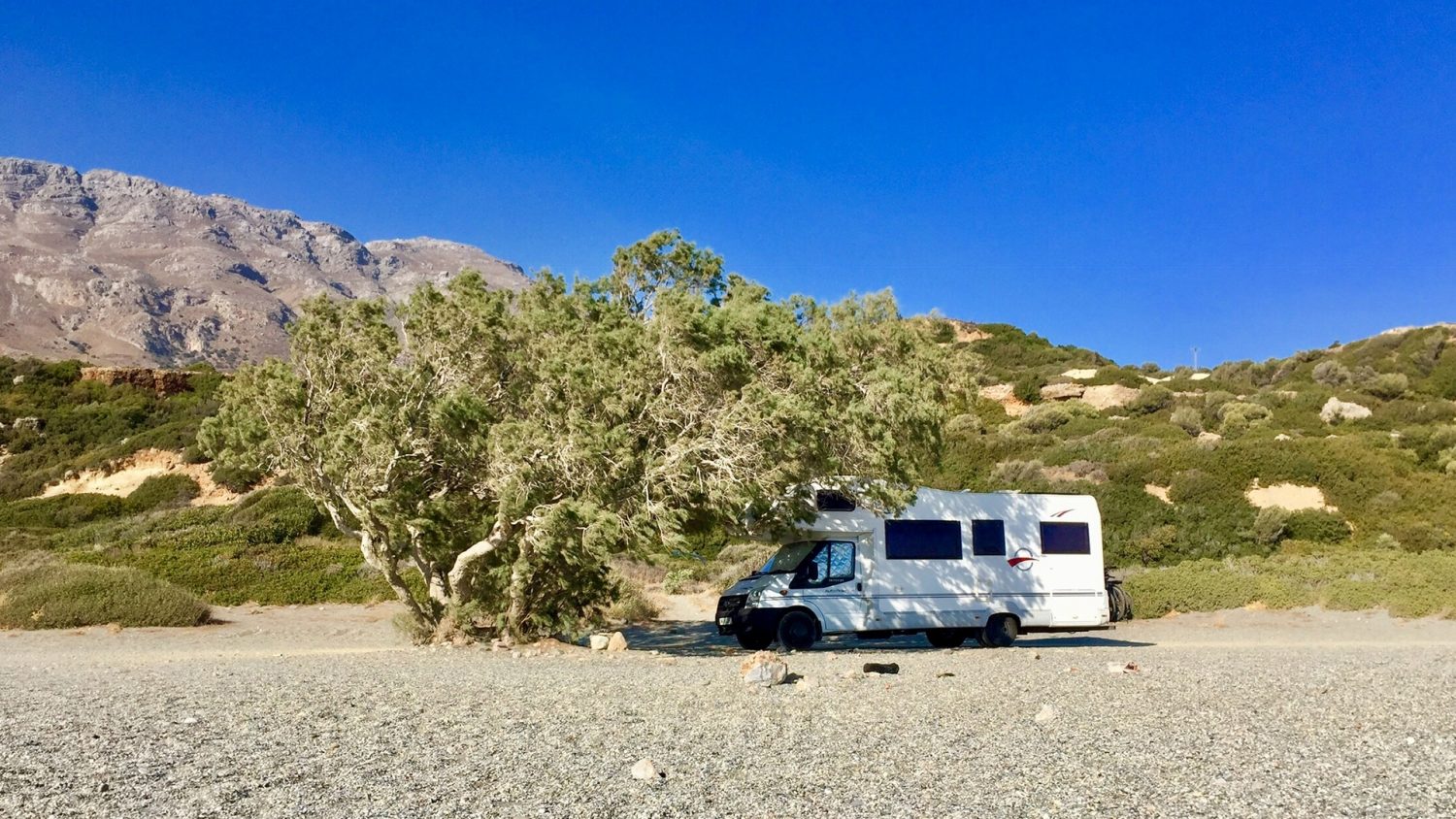 Motorhome parked up on a beach in summer under a tree.